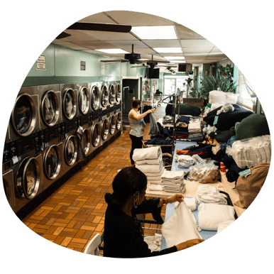 The inside of a laundromat with machines lined up and customers folding clothes.